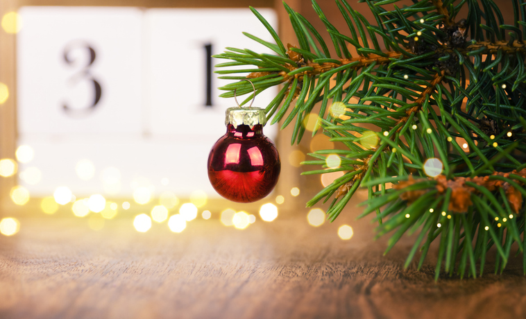 Weihnachtsmärkte in der Vorderpfalz. Weihnachtsbaum mit roter Kugel auf einem Holztisch und Adventskalender mit unscharfen Lichtern im Hintergrund.
