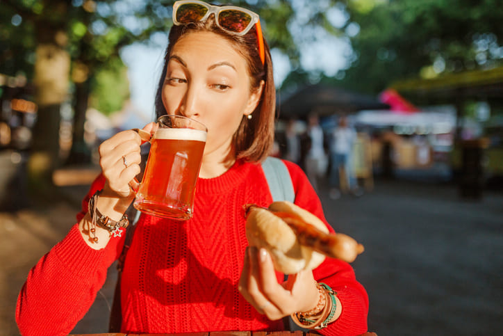 Junge glückliche asiatische Reiseleiterin trinkt Becher Bier mit Hotdog in Deutschland.