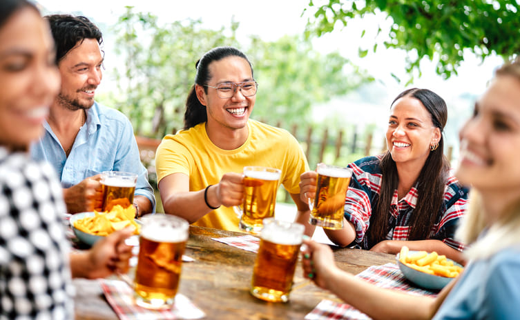 Junge glückliche Freunde, die Bier in einem Biergartenr trinken und anstoßen.