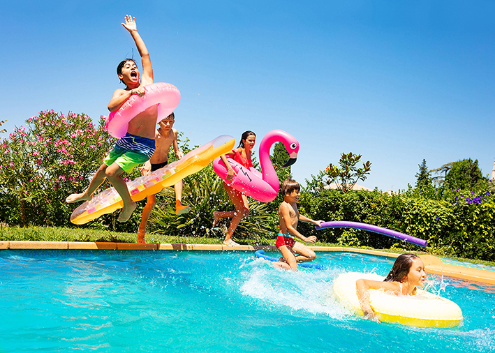 Jugendliche springen mit Schwimmreifen im Freibad ins Becken.