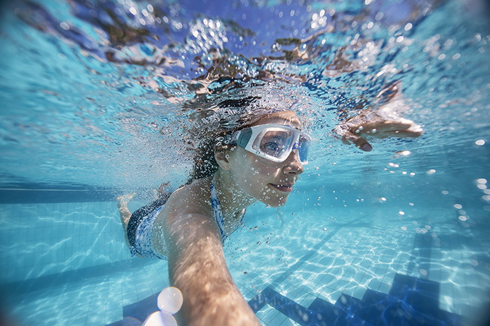 Frau taucht mit Taucherbrille im Schwimmbecken im Freibad.