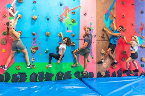 Junge Erwachsene klettern lachend an einer bunten Indoor-Kletterwand, ein Indoor-Tipp in der Vorderpfalz